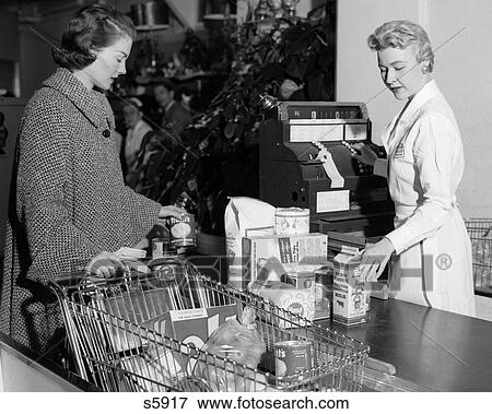 Stock Photo - 1950S Woman At Grocery Store Checkout Counter Handing Items Over For Cashier To Ring Up On Cash Register . Fotosearch