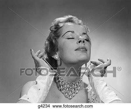 1950S Woman Eyes Closed Chin Lifted Putting On Elaborate Diamond Rhinestone Necklace View Large Photo Image Picture - 1950S Woman Eyes Closed Chin Lifted Putting On Elaborate Diamond Rhinestone Necklace . Fotosearch