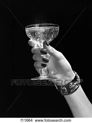Picture - 1950S Woman Hand Ornate Metal Bracelet Holding Up Toast Glass Of Champagne Against Black Background Alochol Liquor New Year. Fotosearch