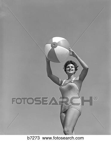 1950S Woman In One Piece Bathing Suit Holding Beach Ball Above Head Looking Down At Camera View Large Photo Image Stock Image - 1950S Woman In One Piece Bathing Suit Holding Beach Ball Above Head Looking Down At Camera . Fotosearch