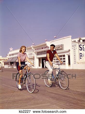 1950S Young Couple Riding Bikes On The Boardwalk Jersey Shore Vacation Summer Man Woman Seaside View Large Photo Image Stock Photo - 1950S Young Couple Riding Bikes On The Boardwalk Jersey Shore Vacation Summer Man Woman Seaside . Fotosearch