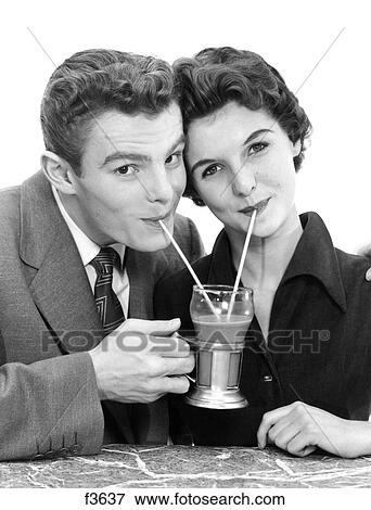 Stock Photo - 1950S Young Couple Smiling At Camera Heads Together Sipping A Single Soda Milkshake With Two Straws . Fotosearch