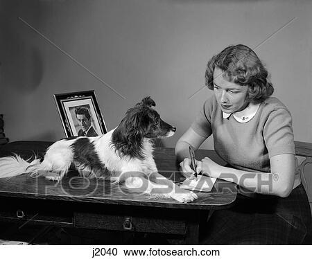Stock Image - 1950S Young Teen Girl At Desk Writing Fan Letter Spotted Dog Lying On Desk Framed Photo Of Man . Fotosearch