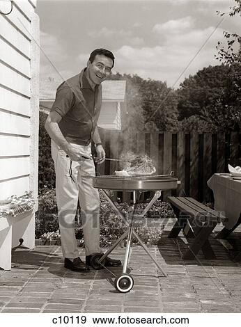 1960S Head-On View Of Man In Backyard Patio Cooking Steak On Grill View Large Photo Image Stock Photo - 1960S Head-On View Of Man In Backyard Patio Cooking Steak On Grill . Fotosearch