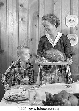 1950S Woman In Apron Putting Turkey On Table With Son Looking On Eagerly View Large Photo Image Picture - 1950S Woman In Apron Putting Turkey On Table With Son Looking On Eagerly . Fotosearch