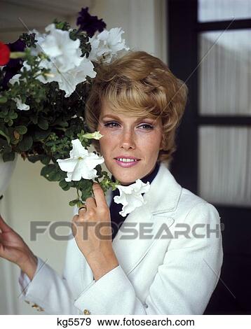 1960 1960S 1970 1970S Smiling Blonde Blond Woman White Jacket Hanging Basket Of Petunias Portrait Flowers View Large Photo Image Stock Photo - 1960 1960S 1970 1970S Smiling Blonde Blond Woman White Jacket Hanging Basket Of Petunias Portrait Flowers . Fotosearch