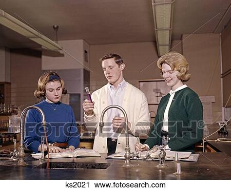 Stock Image - 1960 1960S 3 Students In Chemistry Lab Class Laboratory Experiment Science High School Boy Girls Teens Retro . Fotosearch