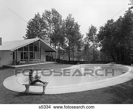 1960 1960S Blonde In Bathing Suit Sitting On Stone Bench With Beach Ball In Lap Near Kidney Shaped Swimming Pool In Backyard View Large Photo Image Picture - 1960 1960S Blonde In Bathing Suit Sitting On Stone Bench With Beach Ball In Lap Near Kidney Shaped Swimming Pool In Backyard. Fotosearch
