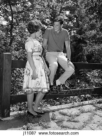 1960 1960S Teenage Couple Talking Dating Sitting Fence Flirting Young Man Woman Date Flirt Conversation Retro View Large Photo Image Stock Photo - 1960 1960S Teenage Couple Talking Dating Sitting Fence Flirting Young Man Woman Date Flirt Conversation Retro . Fotosearch