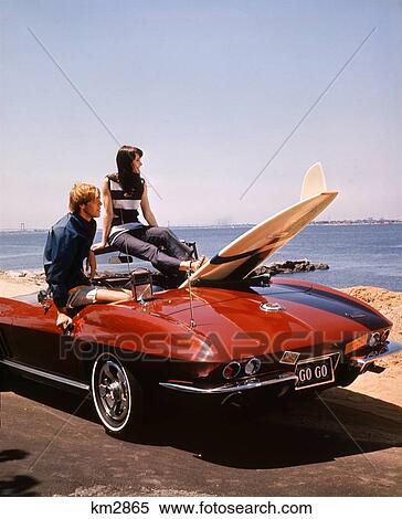 Stock Photography - 1960S 1970S Couple Man Woman Teenage Sitting In Stingray Corvette Surfboard Ocean Beach Outdoor Together Lifestyle . Fotosearch