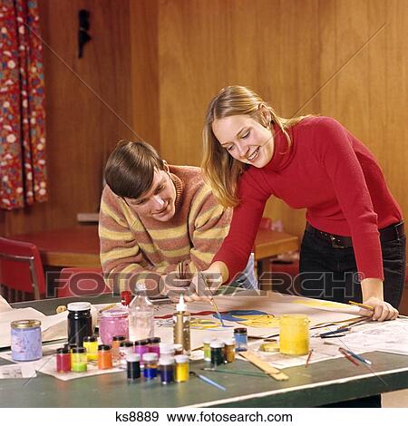Stock Photo - 1960S 1970S Teen Couple Boy Girl Bending Over Table Use Poster Paints Brushes Art & Craft Project Art Class Posters. Fotosearch