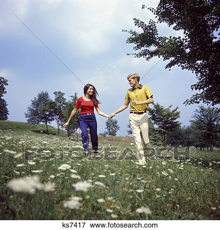 1960S 1970S Young Teen Couple Holding Hands Running Through Field Wild Flowers Queen Annes Lace Romance Fun Fashion View Large Photo Image Stock Photo - 1960S 1970S Young Teen Couple Holding Hands Running Through Field Wild Flowers Queen Annes Lace Romance Fun Fashion. Fotosearch