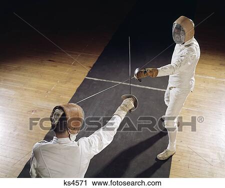 Stock Image - 1960S 2 Men Fencing Crossed Swords Epee Foils Protective Clothing Helmets Wire Face Masks Competition Challenge Retro . Fotosearch