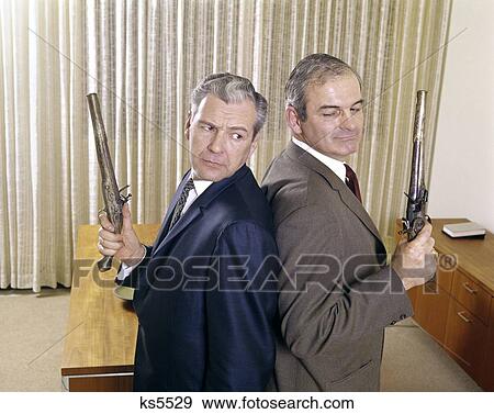 1960S 2 Middle Aged Business Men Stand Back To Back Holding Guns Pistols Duel Duelling Angry Expression Enemy Enemies View Large Photo Image Stock Photo - 1960S 2 Middle Aged Business Men Stand Back To Back Holding Guns Pistols Duel Duelling Angry Expression Enemy Enemies. Fotosearch