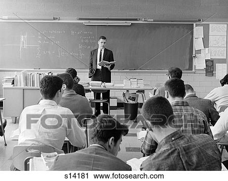 Stock Image - 1960S Back View Of Classroom With Teacher Standing Behind Desk With Book In Hand Explaining Graphed Equation On Blackboard. Fotosearch