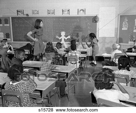 Stock Photo - 1960S Back View Of Grade School Classroom With Teacher At Front Watching Student Working On Blackboard . Fotosearch