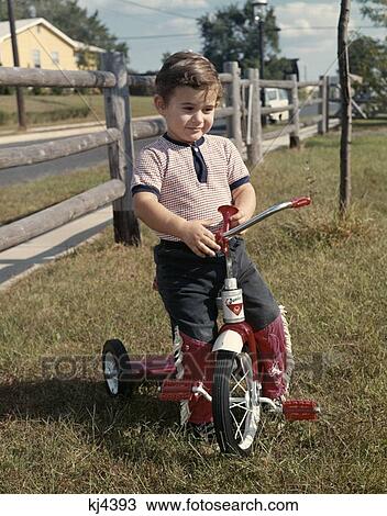 1960S Boy Backyard By Wooden Fence Sit On Red Tricycle Horn On Handlebar Tee Shirt Jeans With Red Cowboy Fringe View Large Photo Image Stock Image - 1960S Boy Backyard By Wooden Fence Sit On Red Tricycle Horn On Handlebar Tee Shirt Jeans With Red Cowboy Fringe . Fotosearch