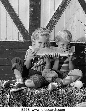 Stock Photo - 1960S Boy Girl Sitting On Bale Of Hay Sharing Eating Slice Of Watermelon Summer Fruit . Fotosearch