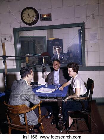 1960s College Radio Station Dj Interview Man Woman Around Microphone At Table On Air Sign Control Room Broadcasting Stock Photograph