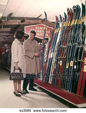 1960S Couple Looking At Skis In Sports Department Store Lifestyle Vacation Man Woman View Large Photo Image Stock Photography - 1960S Couple Looking At Skis In Sports Department Store Lifestyle Vacation Man Woman . Fotosearch
