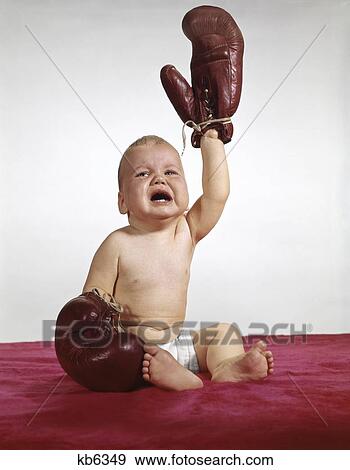Stock Photo - 1960S Crying Baby Wearing Boxing Gloves Holding Up One Arm. Fotosearch