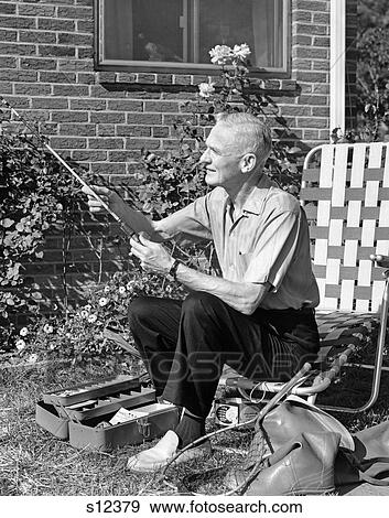 1960S Elderly Man Seated On Lawn Chair Fiddling With Fishing Rod With Tackle Box Net & Rubber Boots At Feet View Large Photo Image Stock Photo - 1960S Elderly Man Seated On Lawn Chair Fiddling With Fishing Rod With Tackle Box Net & Rubber Boots At Feet . Fotosearch