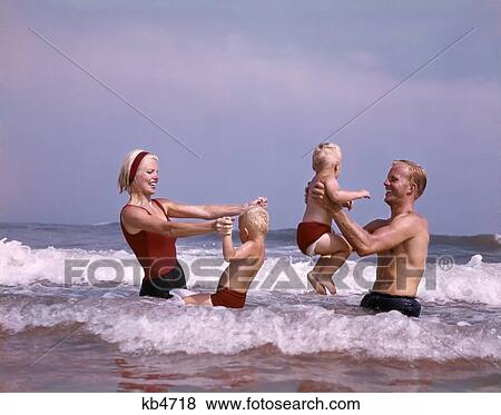 Stock Photo - 1960S Family Father Mother Two Sons Laughing Hand Holding Jumping In Ocean Surf At Beach Having Fun Together. Fotosearch