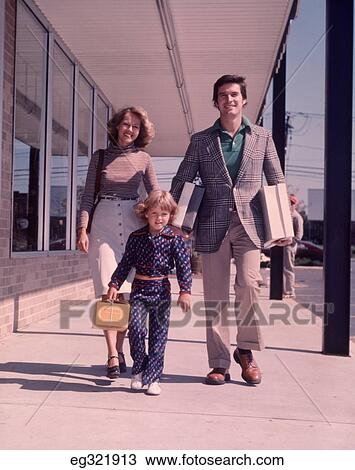 Stock Image - 1960S Family Of 3 Walking Down Street Carrying Packages. Fotosearch