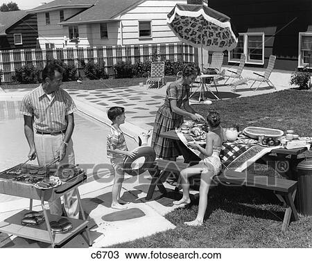 Stock Image - 1960S Family Of 4 In Backyard At Poolside Father Barbecueing & Mother & Children Making Preparations At Picnic Table. Fotosearch
