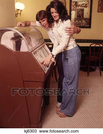 1960S Happy Affectionate Teenage Couple Making Music Selection At Jukebox Boy Girl Song Bell Bottoms Clogs View Large Photo Image Stock Image - 1960S Happy Affectionate Teenage Couple Making Music Selection At Jukebox Boy Girl Song Bell Bottoms Clogs . Fotosearch