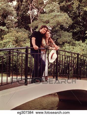 1960S Happy Romantic Couple Outdoors In Park On Footbridge Woman Holding White Hat View Large Photo Image Picture - 1960S Happy Romantic Couple Outdoors In Park On Footbridge Woman Holding White Hat. Fotosearch