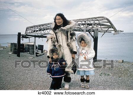 Stock Image - 1960S Inuit Mother Child Eskimo Wearing Parka Anarak Wood Boat Framework Kayak Fur Hood Kotzebue Alaska Native American. Fotosearch