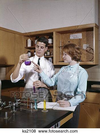 Stock Photo - 1960S Man And Woman College Students In Chemistry Laboratory Looking At Colored Solutions And Writing Notes In Book. Fotosearch