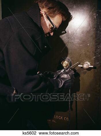 Stock Image - 1960S Man Black Coat Gloves Criminal Holding Drill About To Break Open Safe Crime Safe Cracker Robber Burglar Yegg. Fotosearch