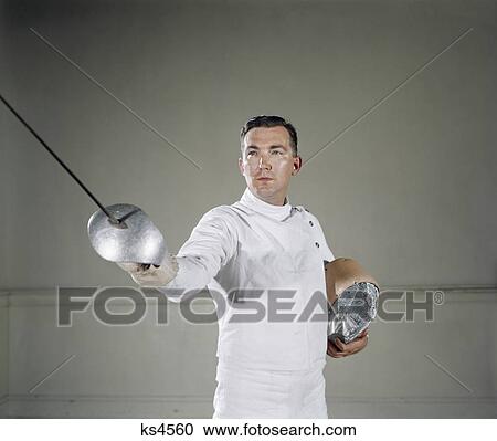 Stock Image - 1960S Man Serious Expression Pointing Epee Sword Holding Helmet Under Arm Fencing Master On Guard Challenge Retro . Fotosearch