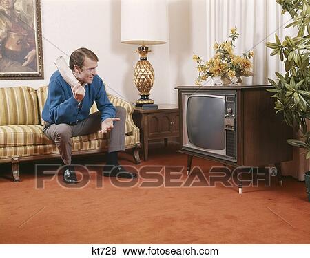 1960S Man Sitting On Sofa Holding Rolled Up Newspaper And Looking At Television Living Room Indoor View Large Photo Image Stock Photo - 1960S Man Sitting On Sofa Holding Rolled Up Newspaper And Looking At Television Living Room Indoor. Fotosearch