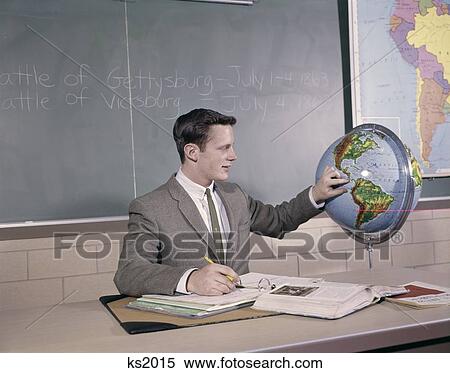 1960S Man Student Teacher Point At Globe At Desk Notebook Book Papers Wear Suit & Tie Chalkboard Study History Geography View Large Photo Image Stock Photography - 1960S Man Student Teacher Point At Globe At Desk Notebook Book Papers Wear Suit & Tie Chalkboard Study History Geography. Fotosearch