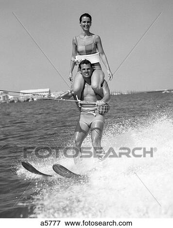 1960S Man Water Skiing With Woman In Bathing Suit Riding On Shoulders View Large Photo Image Stock Photo - 1960S Man Water Skiing With Woman In Bathing Suit Riding On Shoulders . Fotosearch