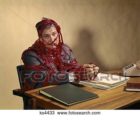 1960S Man Wrapped In Red Tape Sitting At Desk With Hands On Top Of Stack Of Paper Folders View Large Photo Image Stock Image - 1960S Man Wrapped In Red Tape Sitting At Desk With Hands On Top Of Stack Of Paper Folders. Fotosearch