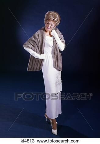 Stock Image - 1960S Middle Aged Blonde Woman In White Gown Fur Stole Wrap Formal Dress On Blue Seamless Photographers Studio Fashion. Fotosearch