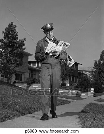 Stock Image - 1960S Postman Delivering Mail Suburban Neighborhood Sorting Letters Walking On Sidewalk. Fotosearch