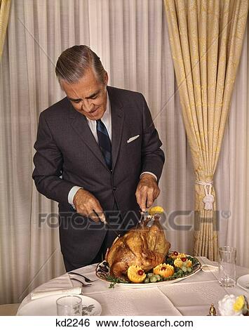 Stock Photograph - 1960S Senior Man Carve Carving Turkey At Dining Room Table Holiday Meal Christmas Thanksgiving Retro Vintage Tradition. Fotosearch