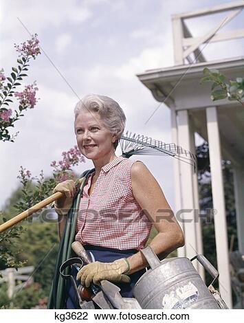 1960S Senior Woman Gardener Holding Rake Hose Watering Can Shovel Tools Wearing Gloves View Large Photo Image Stock Image - 1960S Senior Woman Gardener Holding Rake Hose Watering Can Shovel Tools Wearing Gloves. Fotosearch