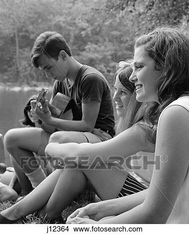 1960S Side View Of Teen Girls Seated On Bank Listening To Teen Boy Play Guitar View Large Photo Image Picture - 1960S Side View Of Teen Girls Seated On Bank Listening To Teen Boy Play Guitar . Fotosearch