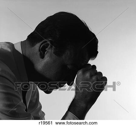 Stock Image - 1960S Silhouetted Man Head Down Hand To Forehead Praying Prayer Depressed Depression Sad Worried . Fotosearch