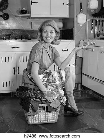 1960S Smiling Housewife In Kitchen Sitting On Top Of Full Laundry Basket Holding Out Hand View Large Photo Image Stock Photograph - 1960S Smiling Housewife In Kitchen Sitting On Top Of Full Laundry Basket Holding Out Hand . Fotosearch
