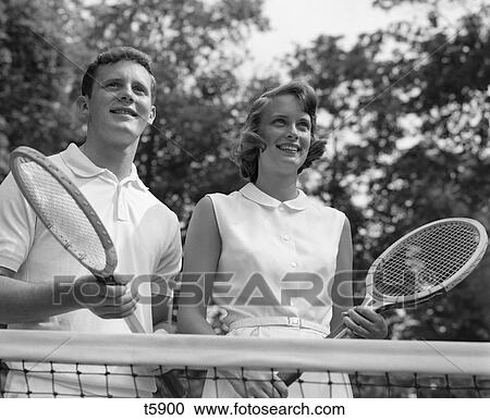 1960S Smiling Portrait Couple Standing Behind Net Holding Racquets View Large Photo Image Stock Image - 1960S Smiling Portrait Couple Standing Behind Net Holding Racquets . Fotosearch