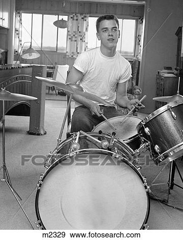 Stock Photo - 1960S Teen Boy With Buzz Cut In T-Shirt Sitting In Front Of Small Drum Kit Holding Sticks Over Snare . Fotosearch