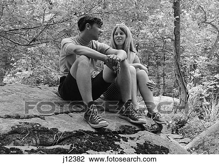 Stock Image - 1960S Teen Couple Sitting On Rock In Woods Talking . Fotosearch