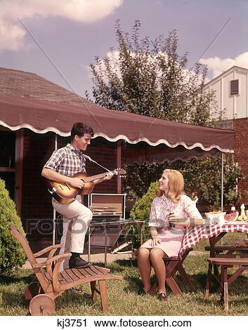 1960S Teenage Boy And Girl At Picnic Table Lunch In Suburban Backyard Boy Playing Acoustic Guitar View Large Photo Image Stock Image - 1960S Teenage Boy And Girl At Picnic Table Lunch In Suburban Backyard Boy Playing Acoustic Guitar . Fotosearch